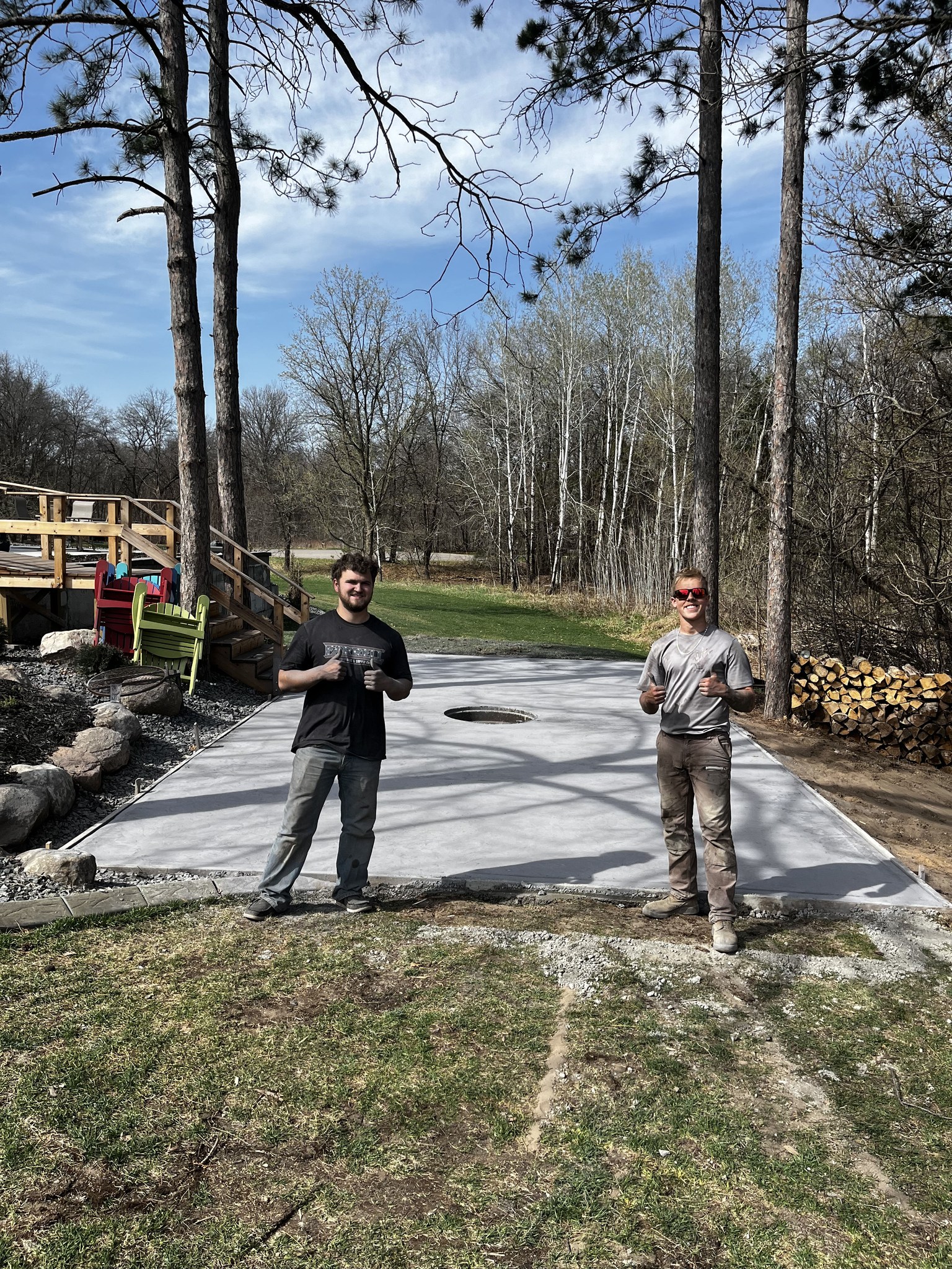 After: stamped concrete patio with stone fire pit, adirondack chairs, and curb edging